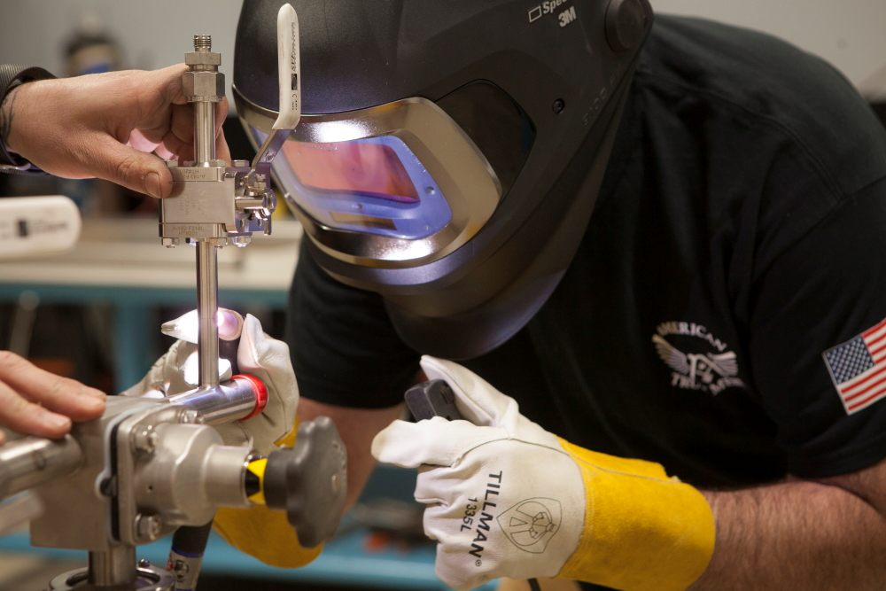 Welder in an auto-darkening helmet welding a stainless steel valve assembly