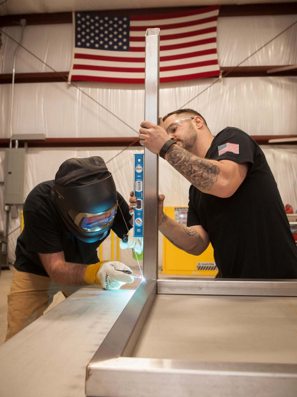 Two fabricators welding and levelling a stainless steel frame in the shop