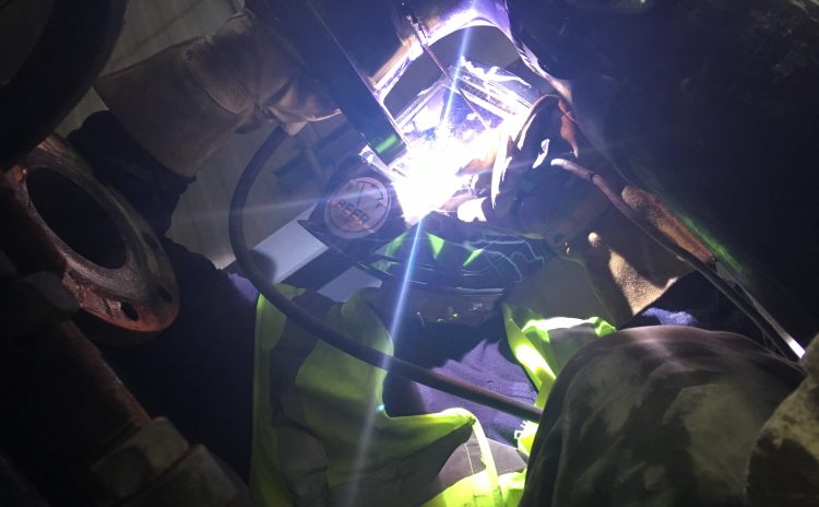 Welder in high-visibility gear welding pipe in a tight space